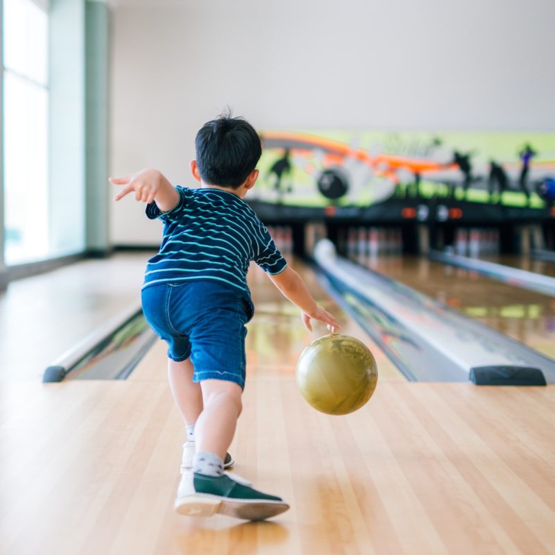 Back view child throwing bowling ball