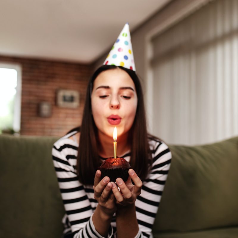 Birthday girl blows out a burning candle on a cupcake